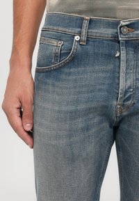Jeans in denim azzurro chiaro con vestibilità dritta, caratterizzati da cuciture arancioni, un classico design a cinque tasche e chiusura anteriore con bottone.