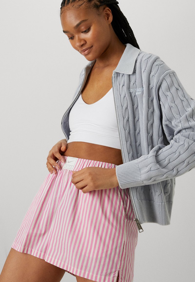 Cardigan en tricot cablé gris clair avec col, associé à une jupe rayée rose et blanche avec une taille élastique et une étiquette logo.