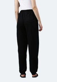 Schwarze lässige Hose mit elastischem Bund und einer Gesäßtasche, lockere Passform und mit Bündchen an den Knöcheln. Aus weichem Stoff gefertigt.