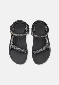 Černé sandály s textilními popruhy s vzorem, nastavitelné pro dokonalé padnutí. Podešev je plochá s texturovaným povrchem pro lepší přilnavost a odolnost.