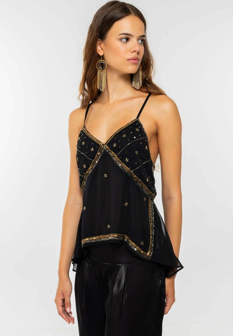 Top negro de gasa con bordado de estrellas doradas y ribete metálico, con tirantes finos y una silueta suelta y asimétrica.