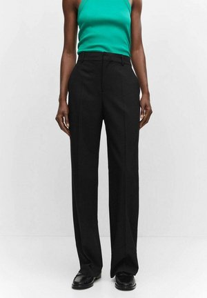 Persoon draagt een zwarte wijde broek met hoge taille, zwarte loafers en een mouwloze turquoise top, tegen een effen witte achtergrond.