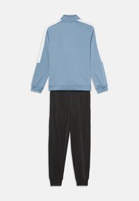Survêtement avec une veste bleu clair dotée d'accents blancs et d'un col haut, associée à un pantalon noir ajusté en tissu lisse.