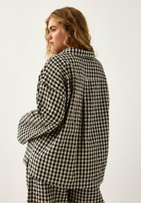Czarna i beżowa kurtka w kratkę gingham o luźnym kroju, z kołnierzem i długimi rękawami. Posiada strukturalną tkaninę oraz detal w postaci szwu na plecach.