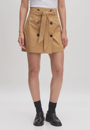 Knie-lange, camel-kleurige rok van katoen. Beschikt over een riem in de taille, een dubbelknopen ontwerp met zwarte knopen en een rechte snit.