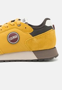 Pantof călărie galben, realizat dintr-o combinație de materiale sintetice și suede. Include un logo rotund, accente texturate și o talpă robustă de culoare maro.