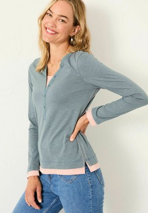 Langarm, hellblaues Oberteil mit Henley-Ausschnitt, Knopfdetails, rosa Akzenten an den Bündchen und dem Saum sowie einer legeren Passform.