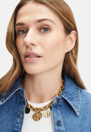 Gouden ketting met ronde hangers, gelaagd over een witte shirt, gecombineerd met een spijkerjack. Glad textuur en glanzende afwerking.