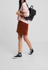 Schwarzer Leder-Rucksack, hellrosa gerippter Pullover, brauner Cord-Minirock und schwarze High-Top-Sneaker mit weißer Sohle und Logo.