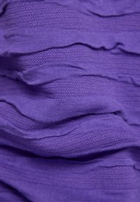 Lila strukturiertem Stoff mit sichtbaren gewellten Schichten, hergestellt aus einem leicht dehnbaren Material, das Tiefe und visuelles Interesse verstärkt.