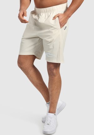 Pantaloni sportivi beige realizzati in tessuto leggero, dotati di vita elasticizzata, tasche laterali e un sottile logo bianco.