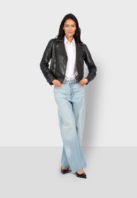 Chaqueta de cuero negra de moto con tachuelas plateadas, camisa blanca de botones, jeans de pierna ancha de color azul claro y bailarinas negras de punta.