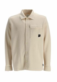 Chemise beige texturée à manches longues avec boutons sur le devant et une poche poitrine boutonnée ornée d’un petit écusson logo noir.