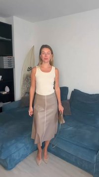 Beige tanktop kombineret med et midi-langt tan-farvet skørt med en central søm; personen holder en lille taske; minimalistisk design, glat tekstur.