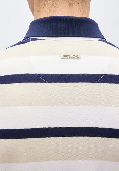 Vue de dos d'une personne portant un polo rayé beige, blanc et bleu marine avec un col bleu marine et un logo métallique RLX sur le haut du dos.