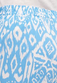 Světle modrá sukni z látky s bílým abstraktním vzorem, s elastickým pasem a hladkou texturou.