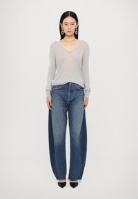 Haut gris à manches longues en V associé à un jean à pattes d'éléphant présentant un design bicolore en denim bleu clair et foncé, souligné par des talons noirs.