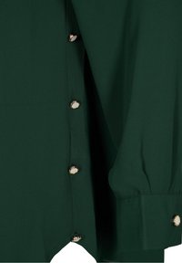 Blusa verde con una texture liscia, dotata di bottoni color oro sul lato e una vestibilità leggermente oversize con maniche arricciate.