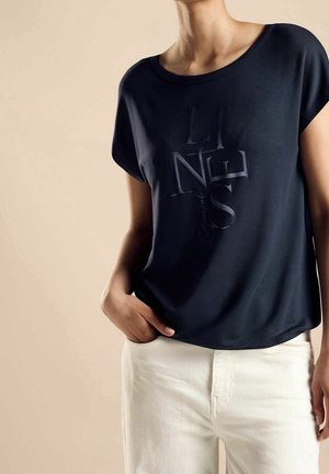 Tmavě modré tričko s krátkými rukávy a texturovaným grafickým potiskem. Měkká látka s volnějším střihem, doplněná bílými kalhotami.