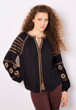 Schwarze Bluse mit langen Ärmeln, mit aufwändiger brauner und goldener Bestickung an den Ärmeln, gebundenem Ausschnitt mit Quasten, lockerer Passform, leichtes Material.