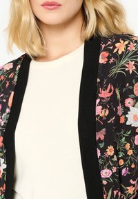 Svart blommig kimono med livfulla flerfärgade blommor, med ett mjukt tyg och öppen framdesign, lagd över en enkel ljus topp.