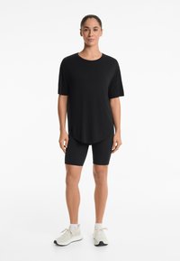 Black T-shirt with short sleeves, round neckline, and curved hem paired with black bike shorts and light athletic shoes.