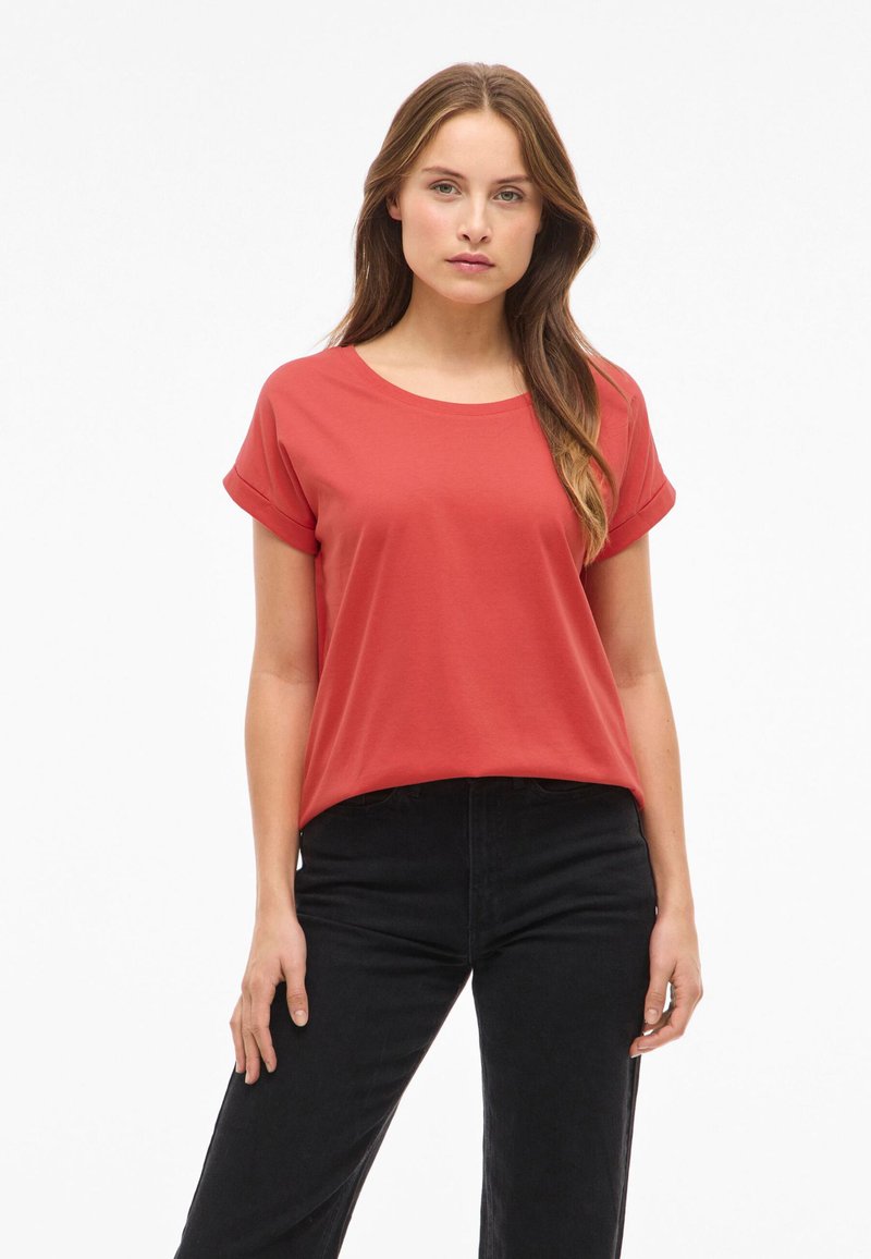 Rød, kortærmet T-shirt lavet af blød bomuld. Har en rund halsudskæring og en afslappet pasform. Sammen med højtaljede sorte jeans.