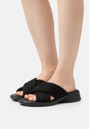 Zwarte slidesandalen met een gestructureerde, gewatteerde bovenkant, voorzien van kruislings gespen en een dikke rubberen zool voor extra comfort.
