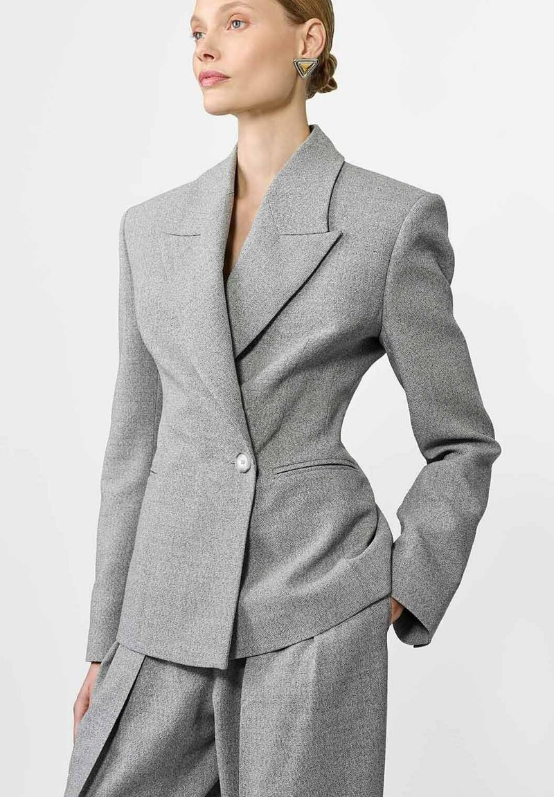 Szary dopasowany żakiet z ostrymi klapami, z jednoprzyciskowym zapięciem i subtelną teksturą, w połączeniu z pasującymi luźnymi spodniami.