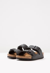 Svarta sandaler med två justerbara remmar och spännen, korkfotbädd och en texturerad gummiussula, med öppen tå och en ergonomisk design.