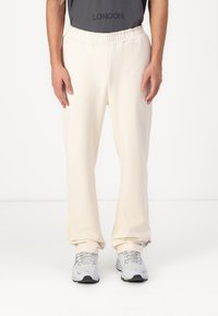 Helle beige Sweatpants mit einem dehnbaren Bund, versehen mit einem subtilen gestickten Logo, aus weichem Stoff gefertigt und an den Knöcheln schmal zulaufend.