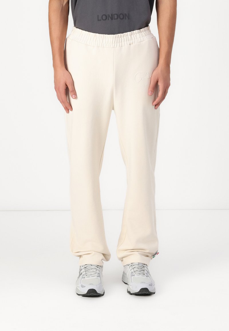 Helle beige Sweatpants mit einem dehnbaren Bund, versehen mit einem subtilen gestickten Logo, aus weichem Stoff gefertigt und an den Knöcheln schmal zulaufend.
