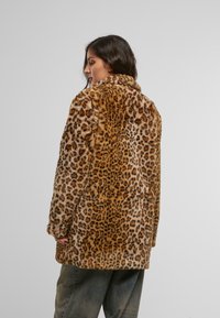 Leopardmønstret faux fur-frakk med stor krage, med brune og lyse prikker på beige bakgrunn, avslappet passform og teksturert overflate.