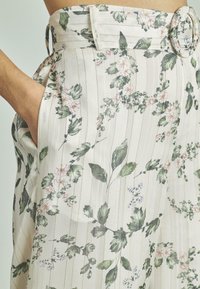 Luchtige rok met hoge taille in een bloemenpatroon, voorzien van groene bladeren en roze bloemen, met verticale strepen en een ronde gesp.
