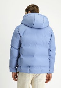 Jasnoniebieska pikowana kurtka z dużym kapturem, o gładkiej fakturze i przeszyciami, w połączeniu z kremowymi spodniami z sztruksu.