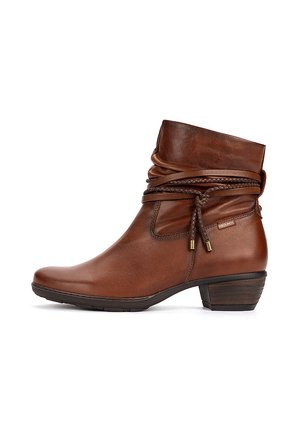 Brown leather ankle boot with low stacked heel, slouchy upper, braided leather straps, and small metallic brand tag on side.