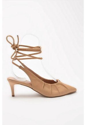 Décolleté beige con tacco kitten, con fasce avvolgenti alla caviglia e dettagli arricciati sulla parte superiore, esposto su uno sfondo bianco.