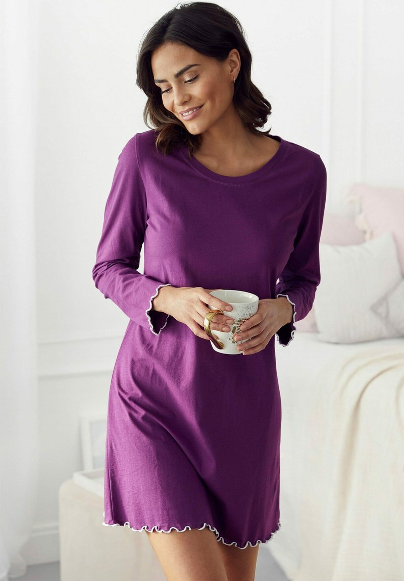 Purple nightdress with long sleeves, a round neckline, and scalloped trim. Smooth fabric with a loose fit, held with a white mug.