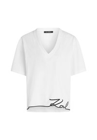 T-shirt bianco corto con scollatura a V e maniche corte. Presenta una firma nera in corsivo sull'orlo inferiore. Tessuto morbido.