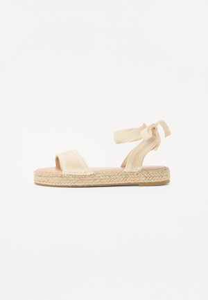 Beige Espadrille-Sandale mit zwei Vorderstraps und einem gebundenen Knöchelriemen. Jutebesockelte Sohle, flaches Design, glatte Stoffoberfläche.