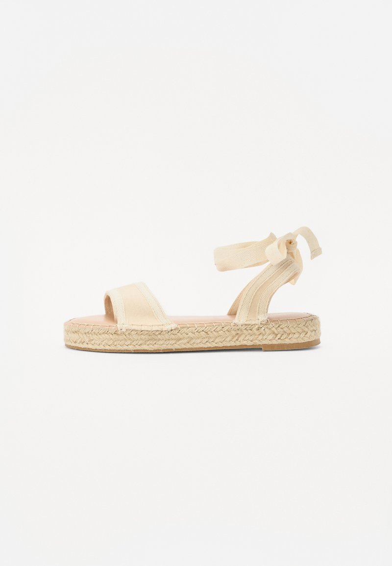 Sandale espadrille beige avec deux sangles avant et une sangle à nouer à la cheville. Semelle enveloppée de jute, design plat, texture de tissu lisse.