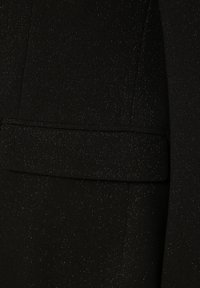 Schwarzer Blazerstoff mit dezentem Schimmer, ausgestattet mit einer strukturierten Tasche und einer glatten Textur. Das Design ist klassisch und maßgeschneidert.