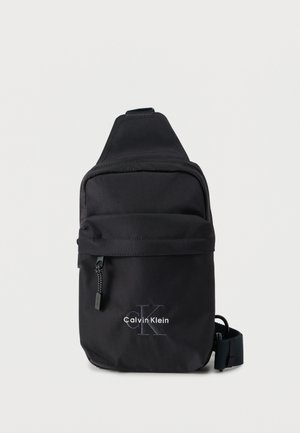 Geantă tip sling neagră din nailon, cu buzunar frontal cu fermoar și curea reglabilă. Prezintă logo-ul „Calvin Klein” brodat alb.