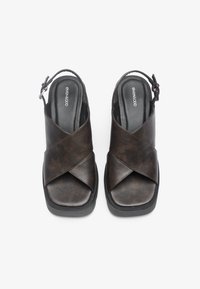 Hnedé kožené sandále na slingback s prekrývajúcim páskovým dizajnom, polstrovanou stielkou a čiernou gumovou podrážkou. Nastaviteľný pásik s detailom pracky.