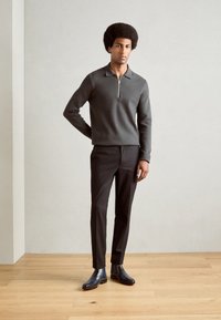 Pulover tricotat gri închis cu guler cu fermoar pe jumătate, asociat cu pantaloni negri ajustați și cizme din piele albastră lustruită până la gleznă.