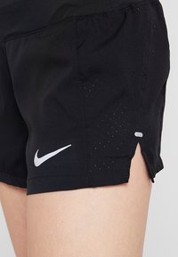 Pantalones cortos deportivos negros con una textura de malla transpirable, una abertura lateral y un logo blanco de Nike en el dobladillo inferior izquierdo.