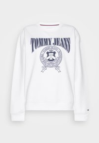 Felpa bianca con logo "TOMMY JEANS" in blu navy, dotata di un emblema circolare e strisce orizzontali al collo. Tessuto morbido con design sportivo.