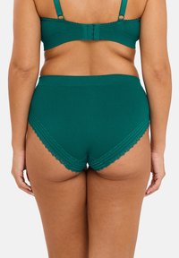 Sous-vêtements taille haute côtelés en bleu sarcelle foncé avec une finition en dentelle décorative sur les bords, présentant un design sans couture et un tissu doux et texturé.