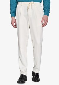 Hvide plisserede bukser med en glat tekstur og en snoreliv, parret med sorte polerede sko og en blå strikket sweater.