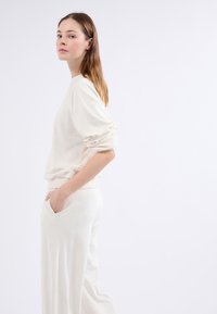 Maglione di colore crema, morbido al tatto, con maniche lunghe e dettagli arricciati, abbinato a pantaloni morbidi dello stesso colore con tasche laterali.